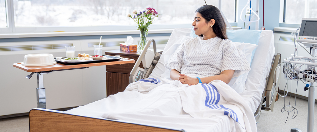 Patient laying in a hospital bed next to a tray of food.