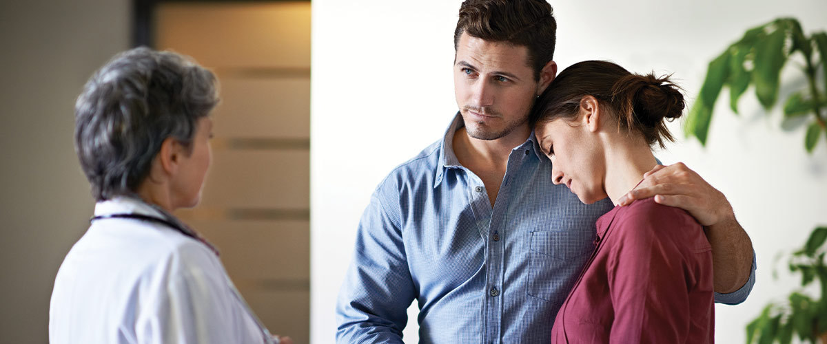 Man comforting a woman while getting news from a doctor.